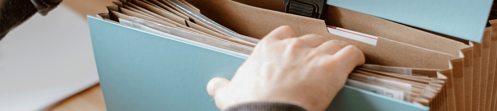 Close up of a hand thumbing through an expandable file folder.