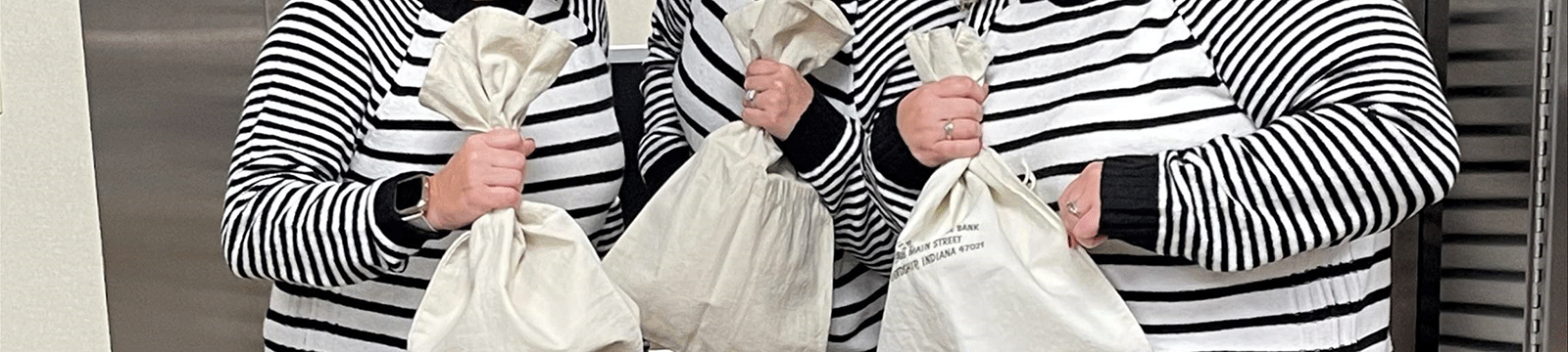 Close up of three individuals wearing black and white striped shirts and holding money bags.