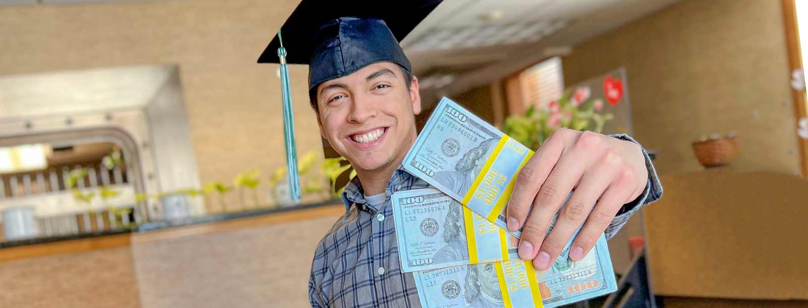 Young man in graduation cap holding $3000 in scholarship money.