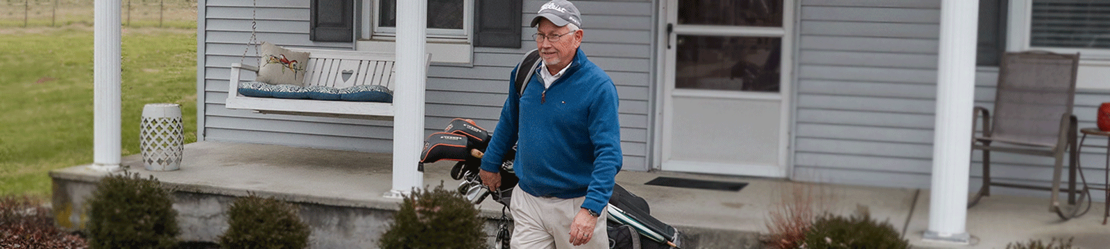 Man carrying golf bag and walking off his front porch.