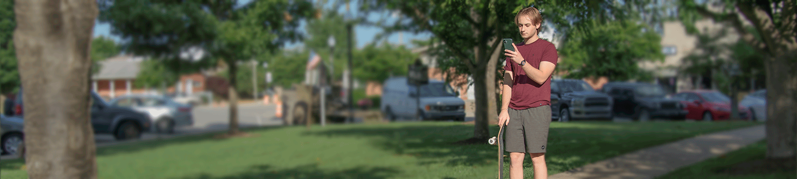 College student holding his skateboard while reviewing his bank accounts on his smartphone.