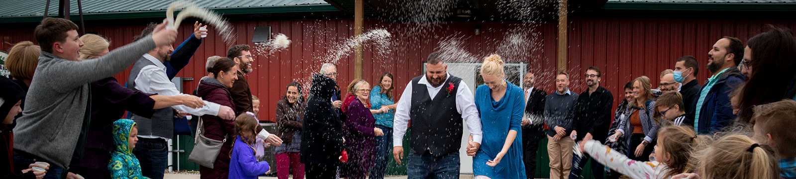 Man and woman leaving wedding venue while guests toss rice.
