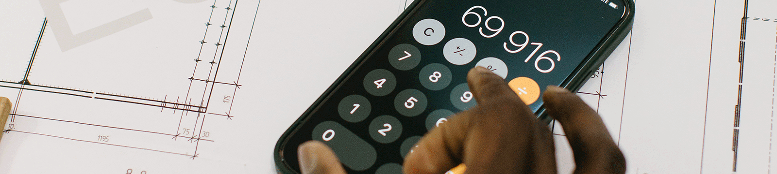 Close up of a person using an iphone calculator sitting on blueprints.