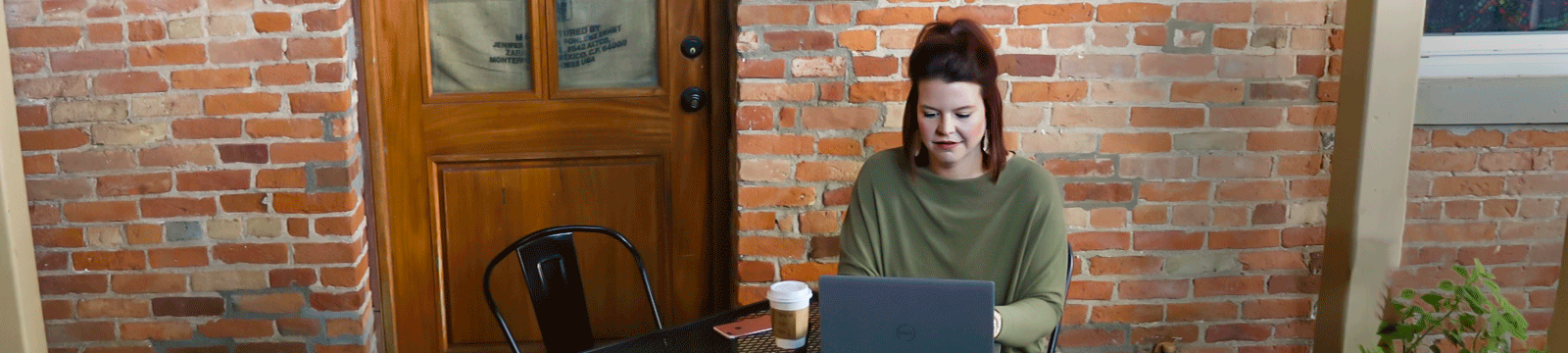 A woman drinking coffee and sitting outside on a patio looking at her laptop.