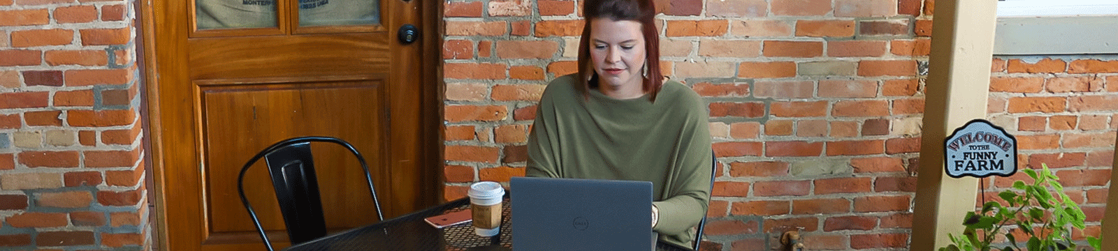 Woman sitting on a patio with coffee looking at laptop.